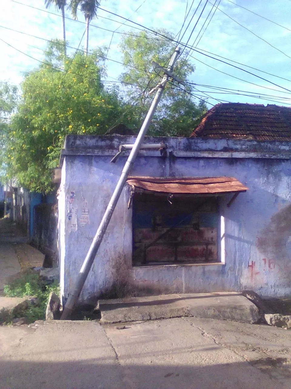 கடையின் மீது சாய்ந்த இரும்பு கம்பம் கடையின் மீது சாய்ந்த இரும்பு கம்பம்